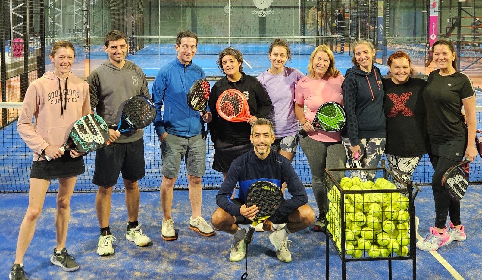 Equipo de un club posando con sus paletas en la cancha después de una clínica de pádel